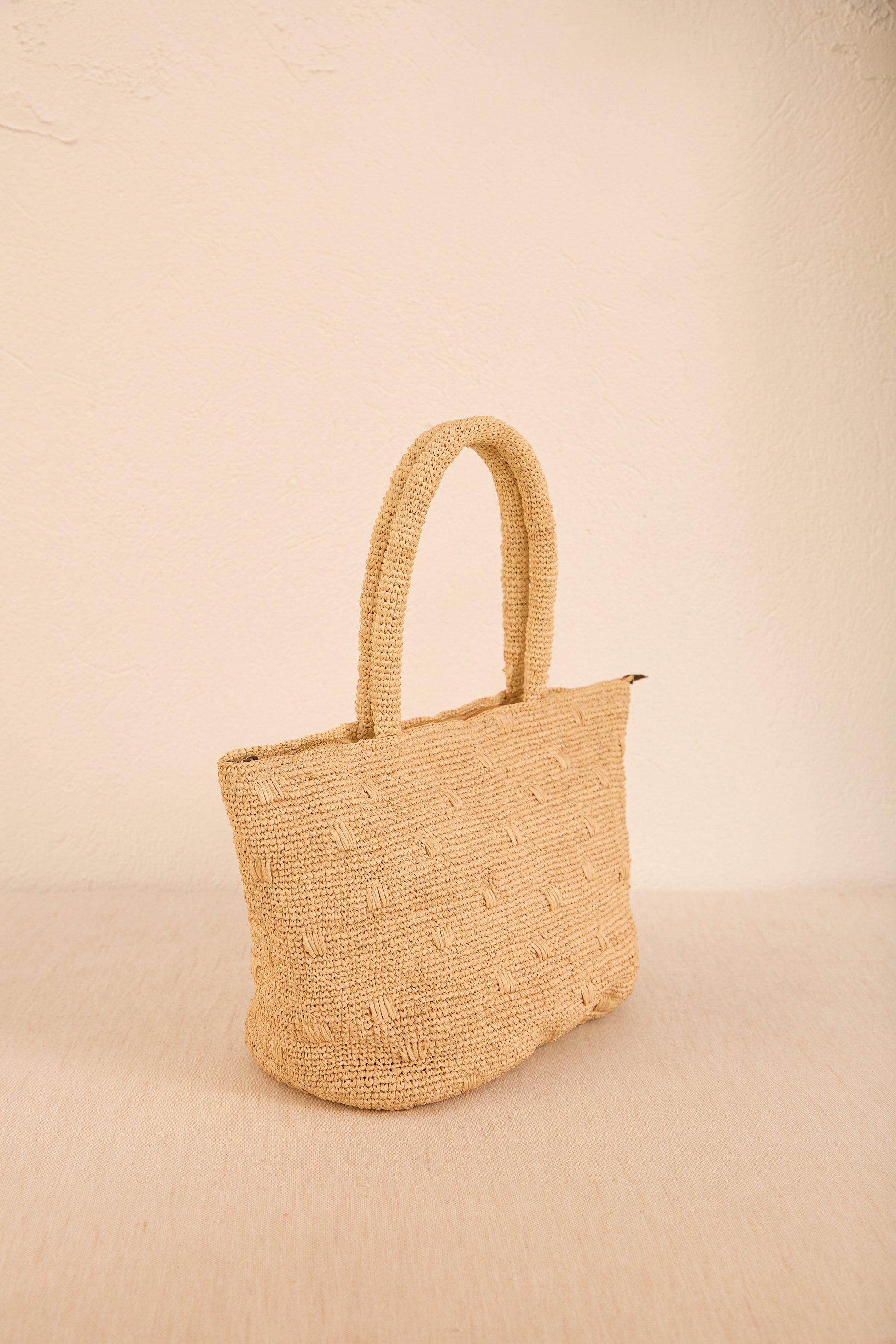 Vista lateral da bolsa 'Gota', destacando seu formato curvilíneo e alça em palha, ideal para looks despojados e elegantes.