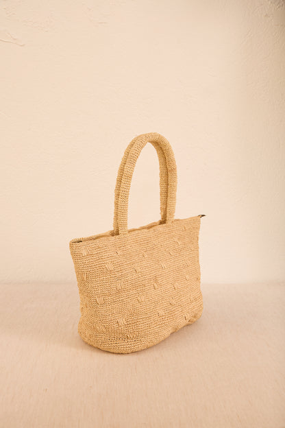 Vista lateral da bolsa 'Gota', destacando seu formato curvilíneo e alça em palha, ideal para looks despojados e elegantes.